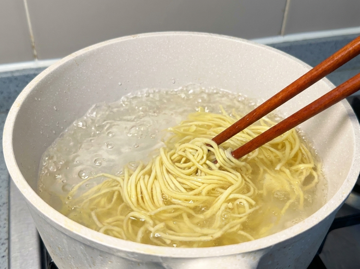 끓는 물에서 노란 라멘 생면을 젓가락으로 들어 올리는 모습.