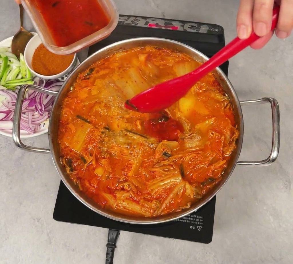 보글보글 끓는 찌개에 빨간 김칫국물을 넣는 모습