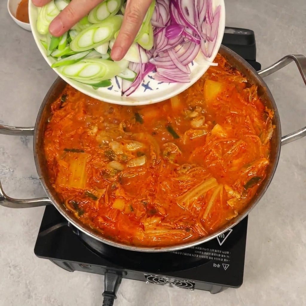 끓는 찌개에 썰어둔 양파와 대파를 밀어 넣는 모습