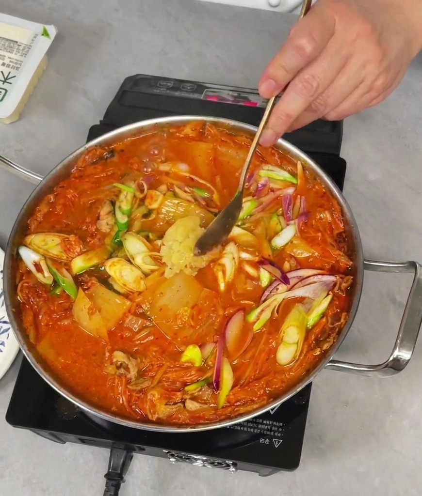 끓는 김치찌개에 다진 마늘 한 숟가락을 넣는 모습
