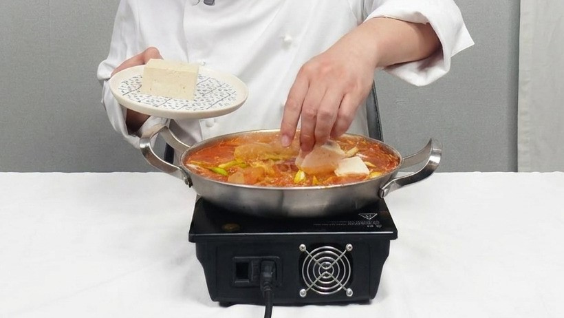 끓는 찌개에 먹기 좋게 썬 두부를 조심스럽게 올리는 모습