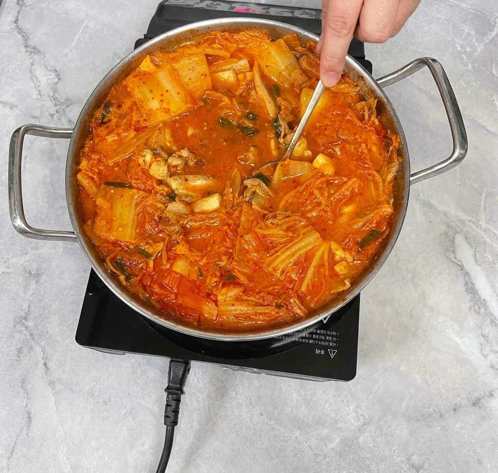 숟가락으로 빨간 김치찌개를 부드럽게 저으며 끓이는 모습