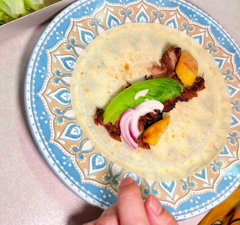 장식용 접시 위에 놓인 또띠아 정중앙에 훈제 소고기, 슬라이스한 아보카도, 적양파가 듬뿍 올려진 모습.