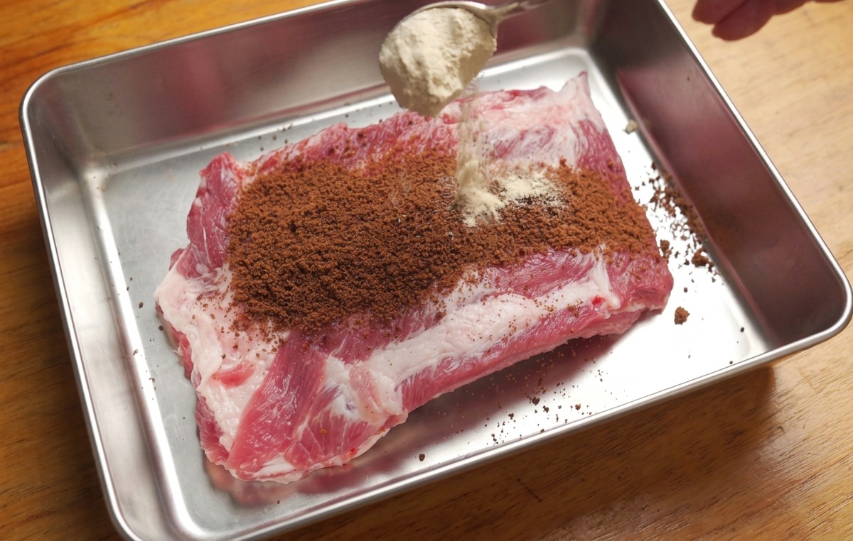 쟁반에 담긴 생 등갈비 위에 황설탕과 혼합 향신료를 숟가락으로 뿌리는 모습.