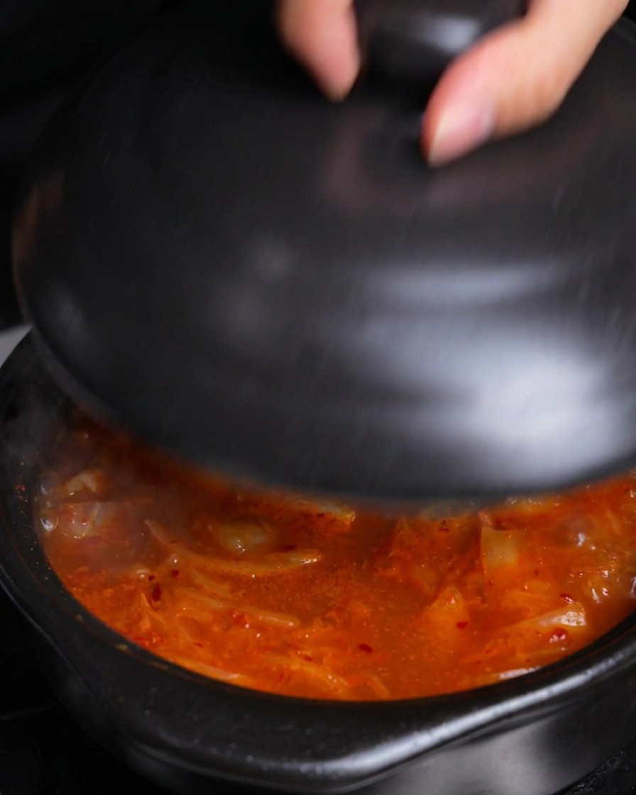 보글보글 끓는 김치찌개 냄비에 검은색 뚜껑을 덮는 모습.