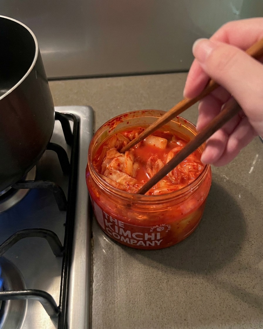 투명한 용기에서 빨갛고 매콤한 김치를 젓가락으로 집어 올리는 모습.