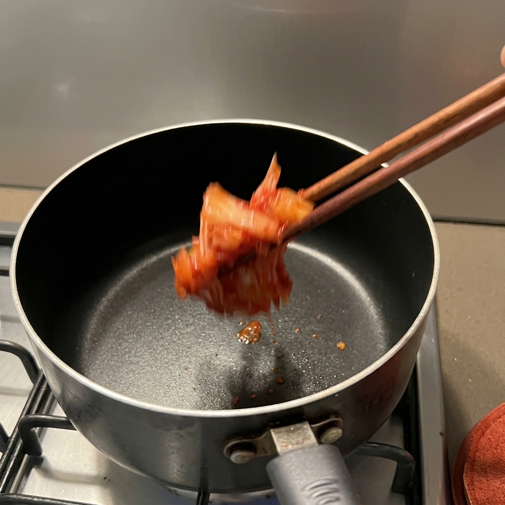 가스레인지 위 냄비에 빨간 김치를 넣고 볶는 모습.