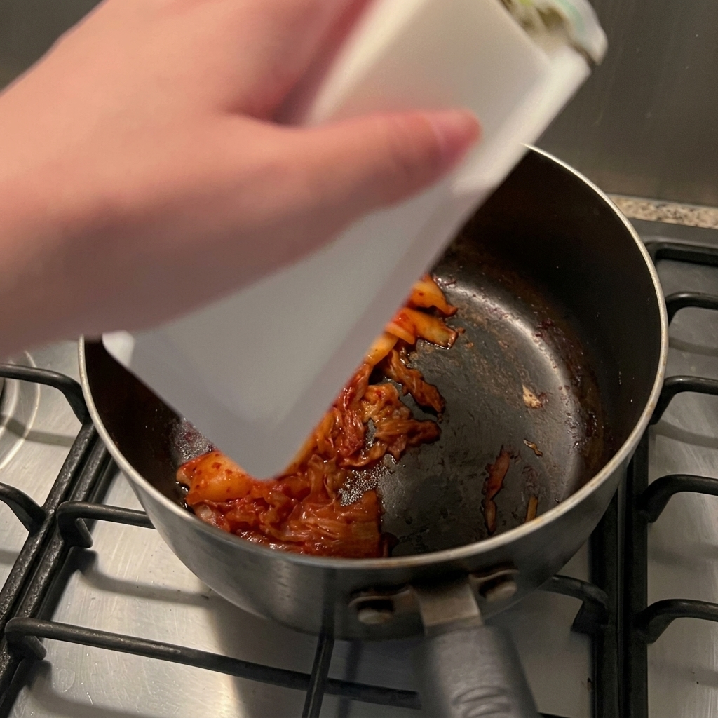 볶은 김치가 담긴 냄비에 하얀 순두부 한 봉지를 통째로 넣는 모습.