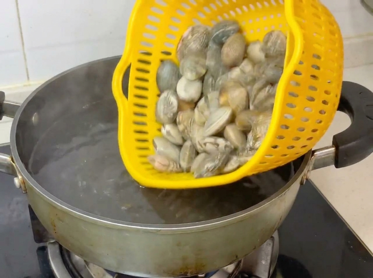 노란 채반에 담긴 생조개를 끓는 물이 담긴 냄비에 붓는 모습.
