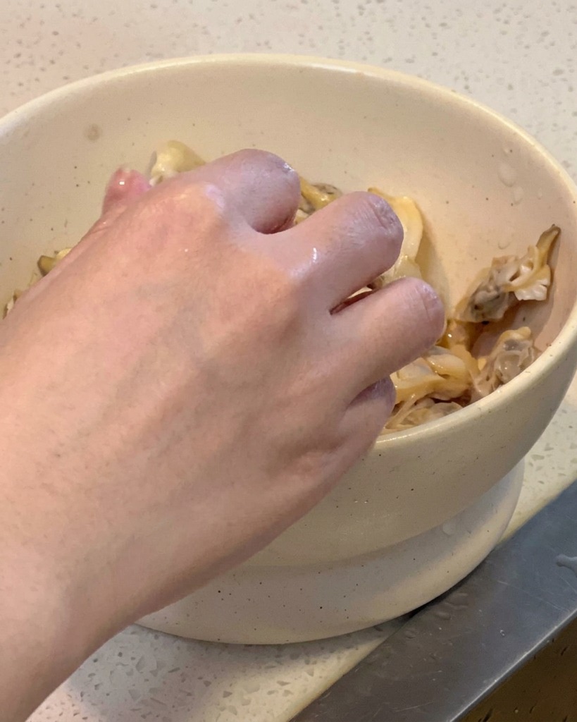 삶은 조개의 껍질을 벗겨 하얀 그릇에 조개 살만 담고 있는 모습.