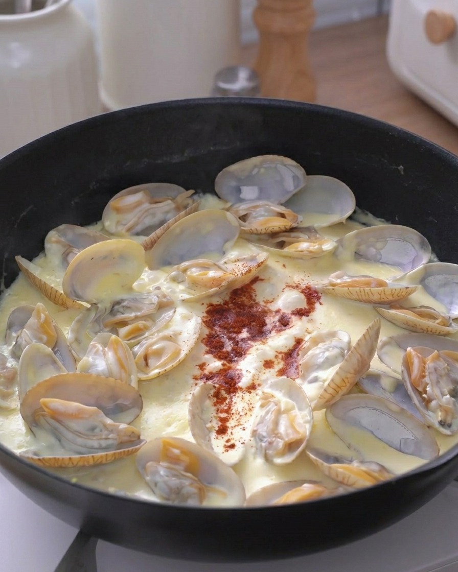 끓고 있는 크림 조개 스튜 중앙에 붉은색 향신료 가루를 뿌리는 모습.