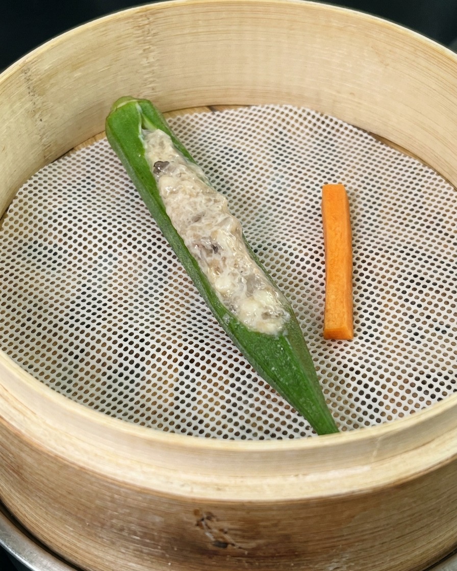 대나무 찜기 안의 흰색 매트 위에 놓인 새우 속을 채운 오크라와 당근 조각.