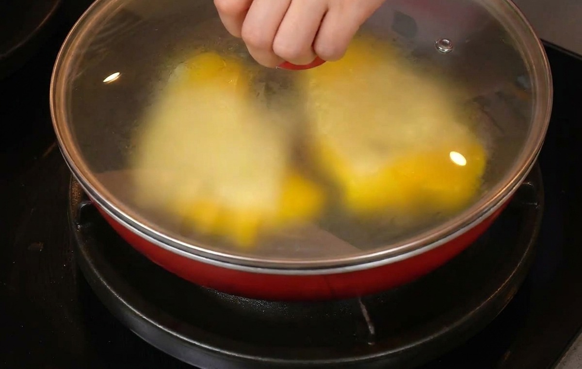치즈가 올라간 스크램블 에그가 담긴 팬에 유리 뚜껑을 덮는 손.