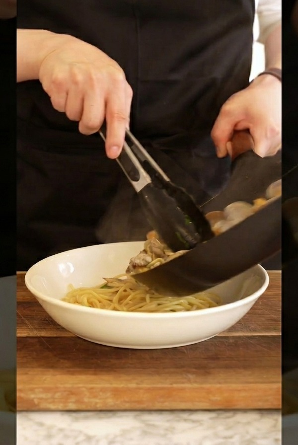 집게로 파스타를 돌돌 말아 그릇에 예쁘게 담는 모습.