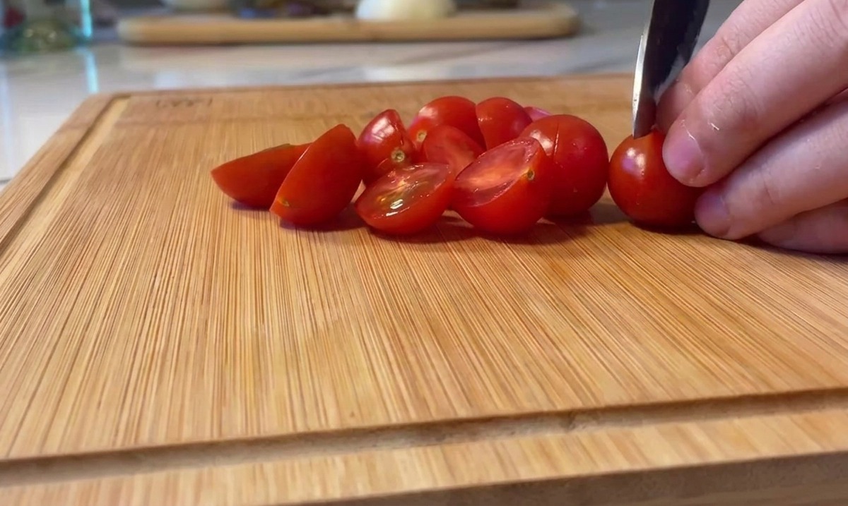 나무 도마 위에서 선홍색 방울토마토를 반으로 자르는 모습.