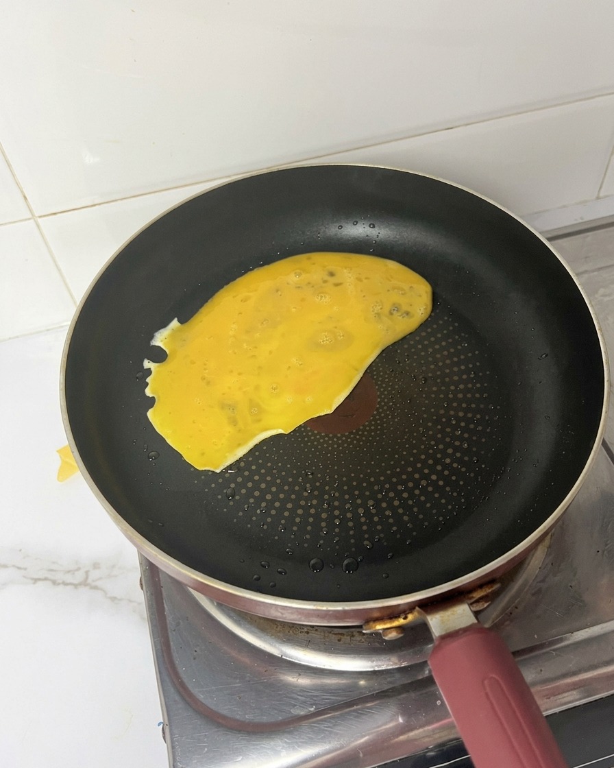 노란 계란물이 뜨거운 검은색 프라이팬 전체에 넓게 퍼지는 모습.