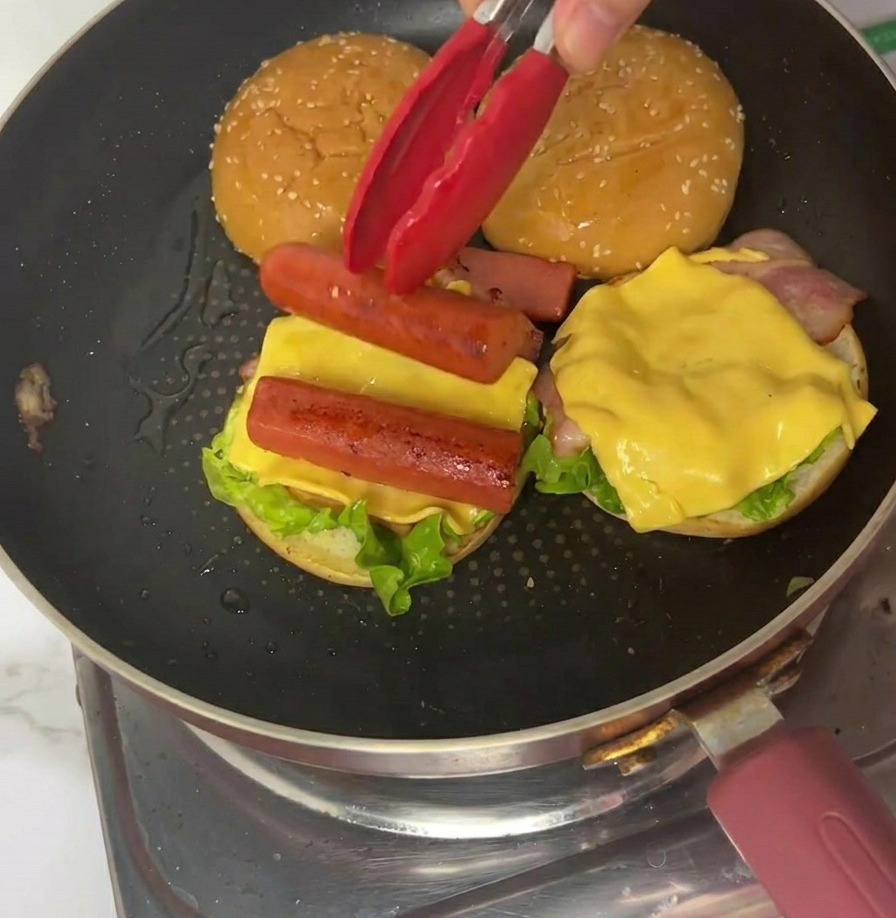 프라이팬에서 빨간색 집게로 4등분한 얇은 오믈렛 한 조각을 버거 위에 올리는 모습.