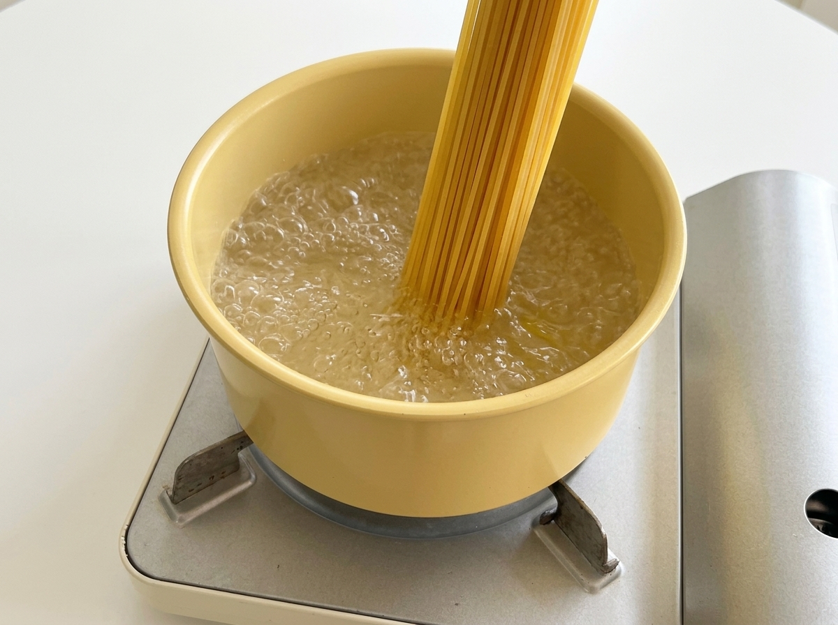 끓는 물이 담긴 노란색 냄비에 마른 스파게티 면을 넣는 모습.