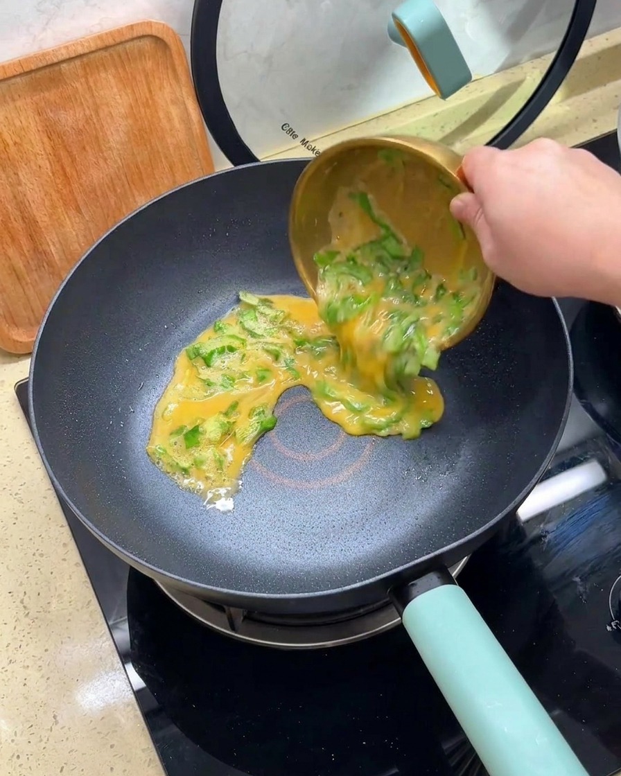 골드 볼에 담긴 계란과 상추 혼합물을 달궈진 논스틱 팬 중앙에 붓는 모습.