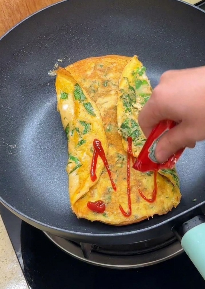 팬 안의 접힌 오믈렛 위에 케첩을 짜서 뿌리는 모습.
