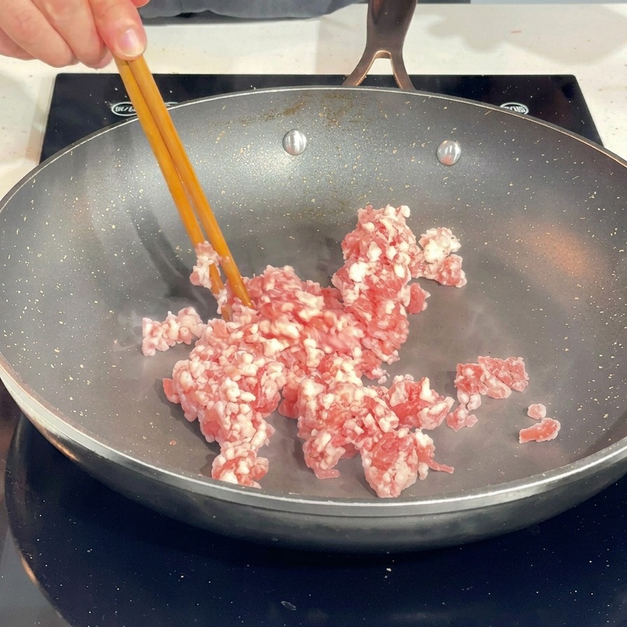 달궈진 프라이팬 위에서 젓가락으로 다진 돼지고기를 풀어주는 모습.