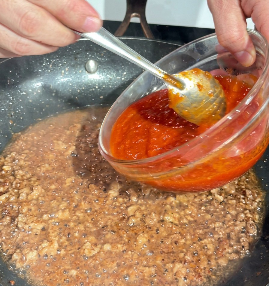 볶은 고기가 있는 팬에 진한 빨간색 토마토 소스를 붓는 장면.