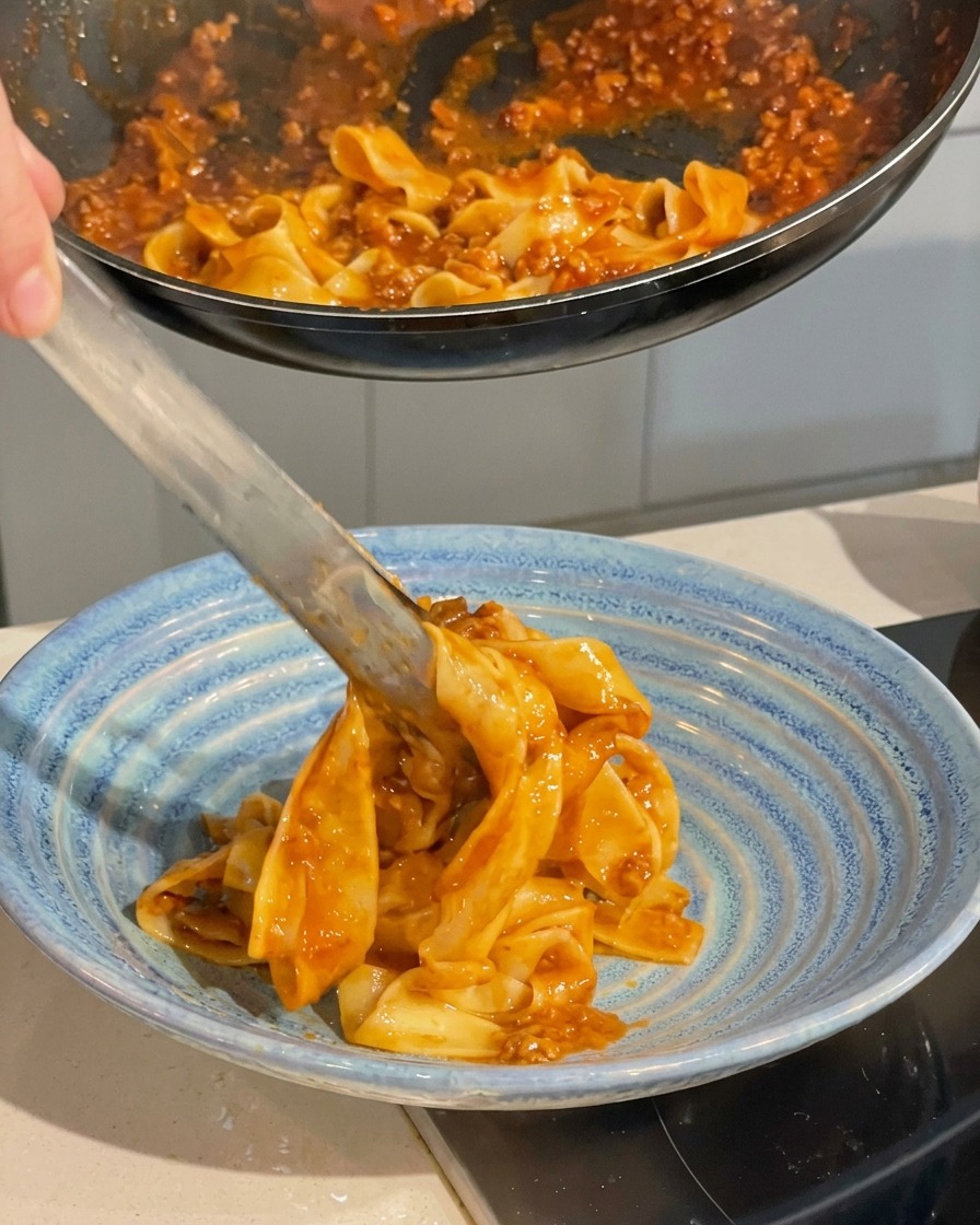 집게로 파스타를 집어 파란색 접시에 정성스럽게 옮겨 담는 모습.