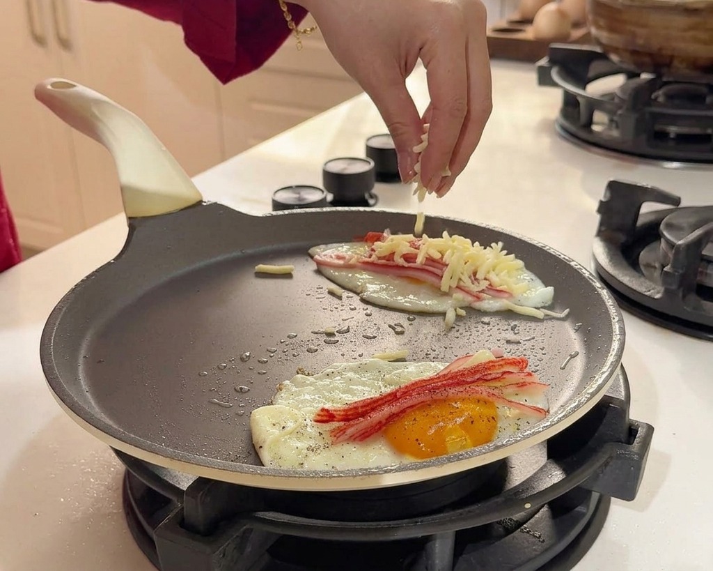 요리 중인 계란과 게살 패티 위에 하얀 슈레드 치즈를 뿌리는 손.