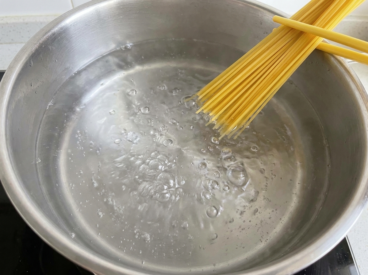 끓는 물에 건조 스파게티 면을 넣고 서서히 잠기게 하는 모습.