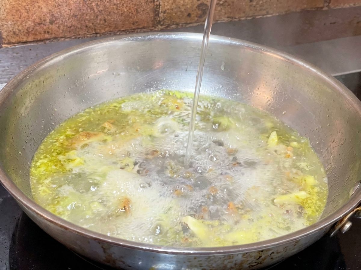 마늘과 오일이 끓고 있는 팬에 면수를 한 국자 붓는 모습.