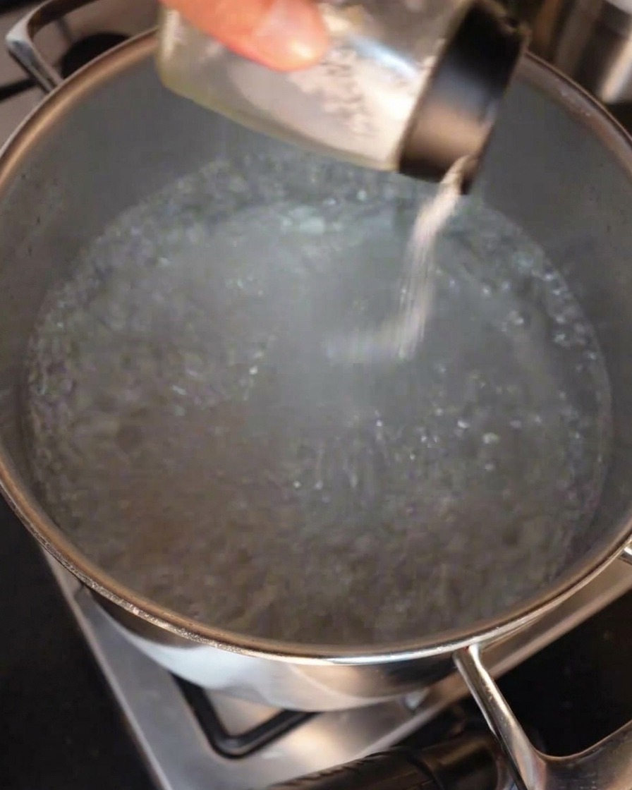 펄펄 끓는 물이 담긴 큰 스테인리스 냄비에 소금을 뿌려 넣는 손