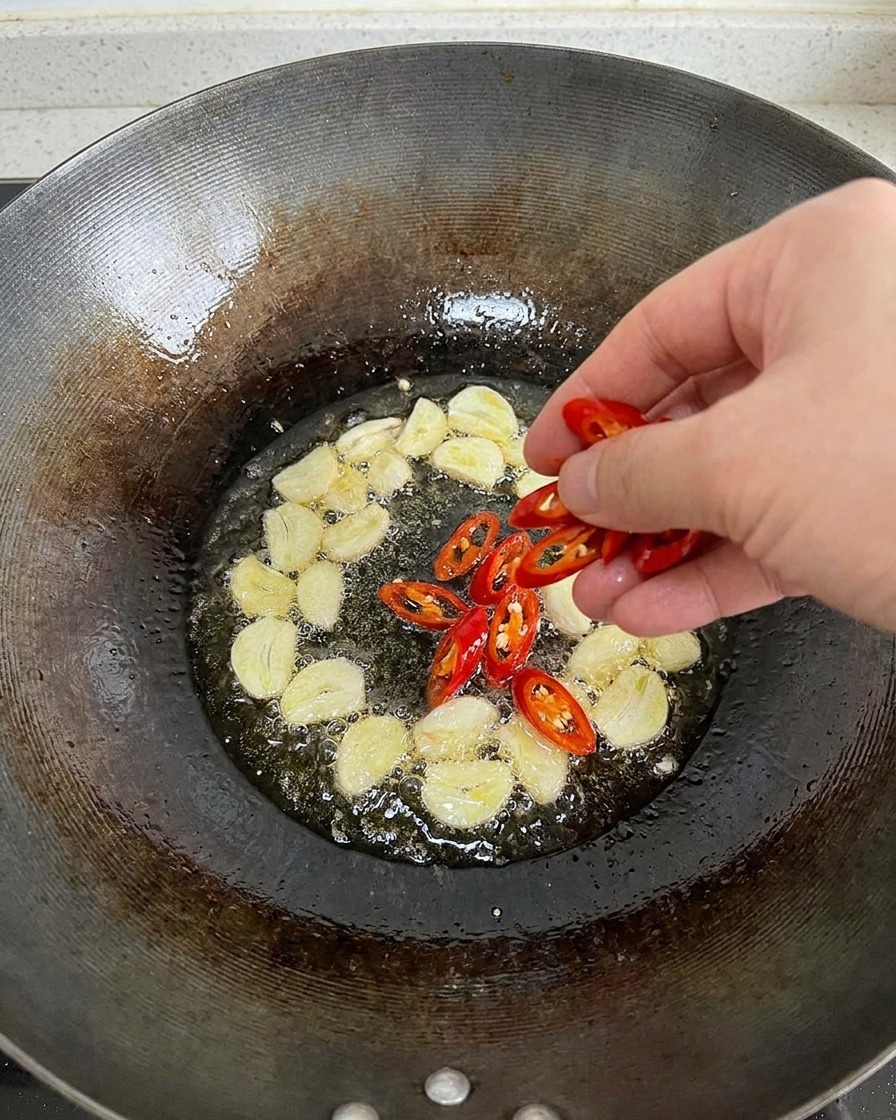 마늘이 끓고 있는 뜨거운 기름이 담긴 웍에 썬 홍고추를 넣는 손