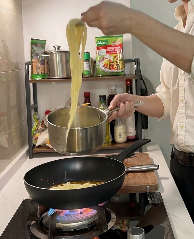 집게를 이용해 냄비에서 삶아진 면을 건져 소스가 담긴 팬으로 옮기는 모습.