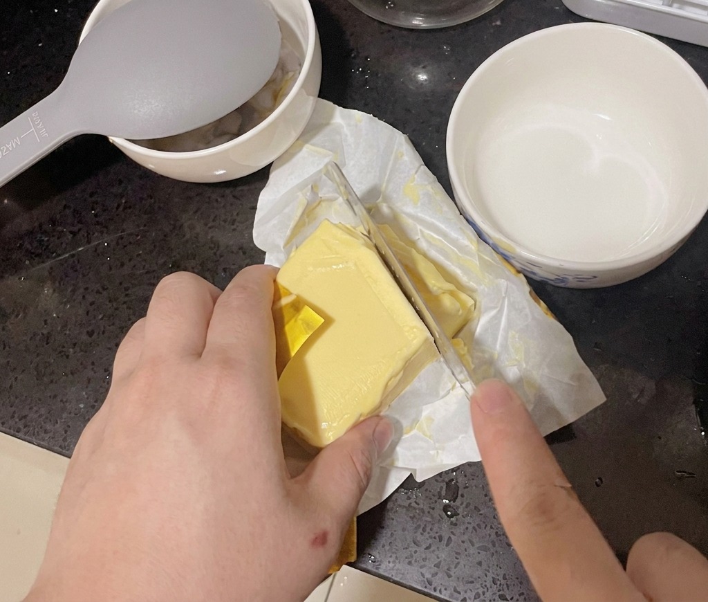 도마 위에서 버터 한 조각을 칼로 자르는 모습