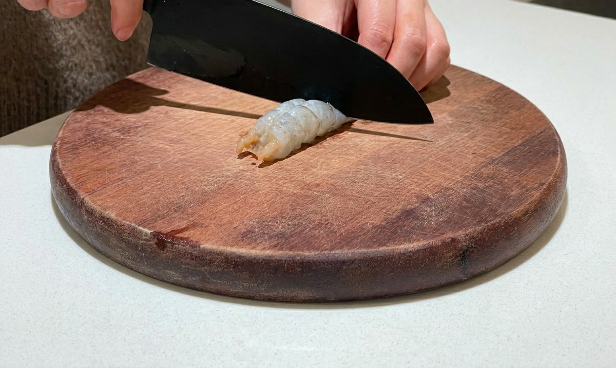 나무 도마 위에서 칼을 이용해 껍질을 벗긴 새우 등 부분을 갈라 내장을 제거하는 모습.