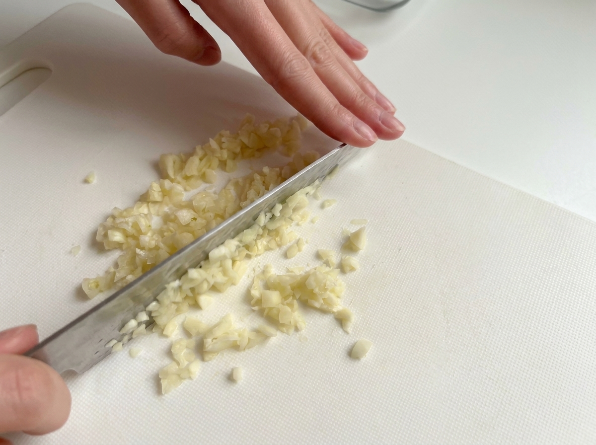도마 위에서 칼로 마늘을 잘게 다지는 모습.