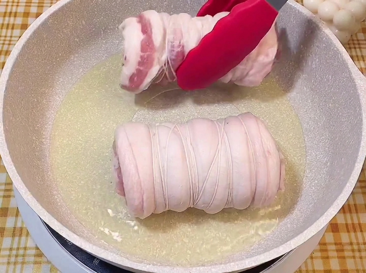 달궈진 팬에 기름을 두르고 실로 묶은 고기를 올리는 장면.