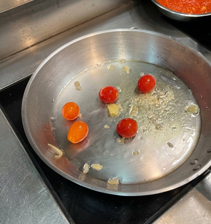 기름에 볶아지고 있는 체리 토마토 위에 레드 페퍼 홀을 뿌리는 모습.