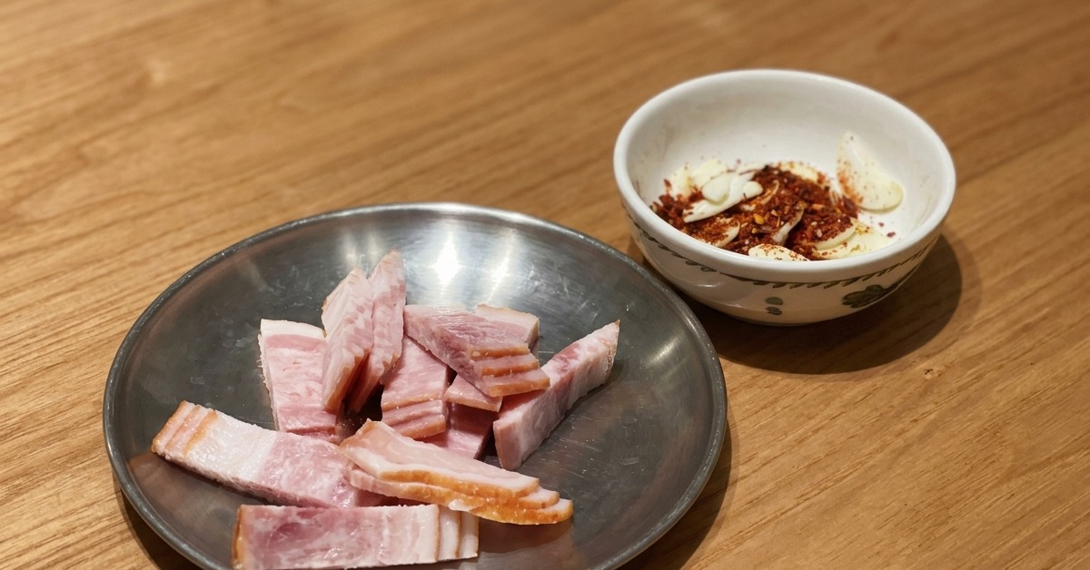 나무 테이블 위 금속 접시에 담긴 베이컨 조각과 마늘 슬라이스, 레드 페퍼 홀.