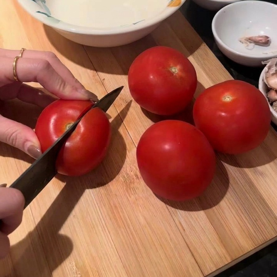 도마 위에서 신선한 토마토를 칼로 썰고 있는 손.