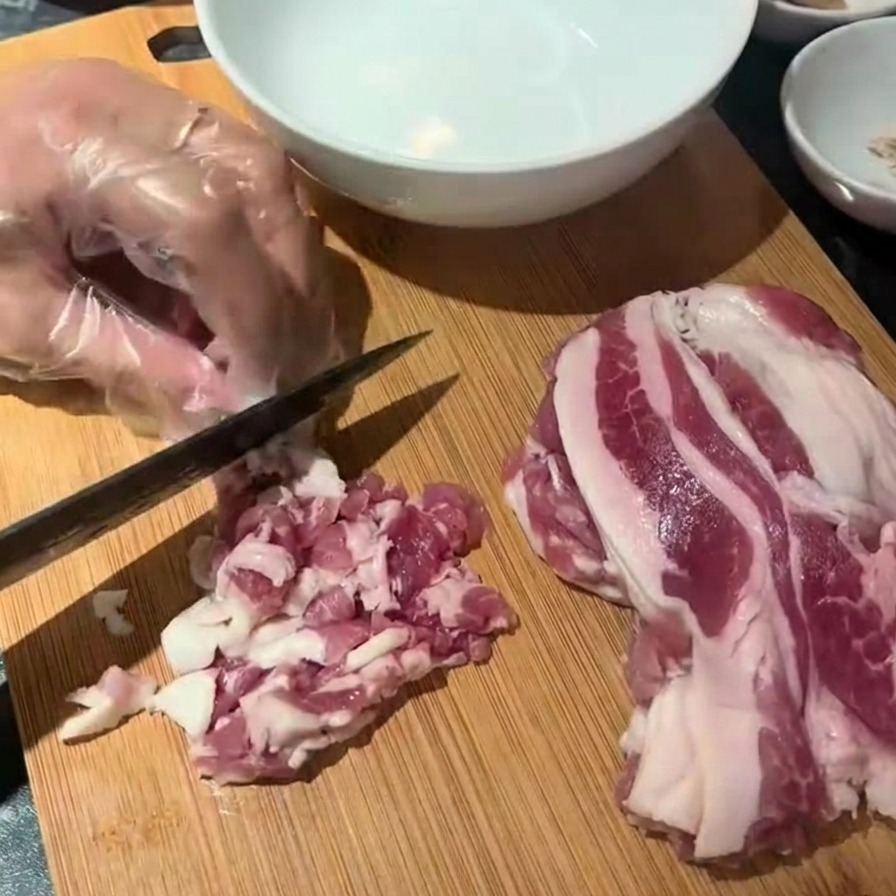 도마 위에서 생베이컨을 한입 크기로 자르고 있는 모습.
