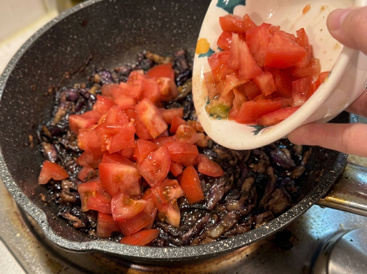 베이컨과 양파가 볶아진 팬에 썰어둔 토마토를 붓는 모습.
