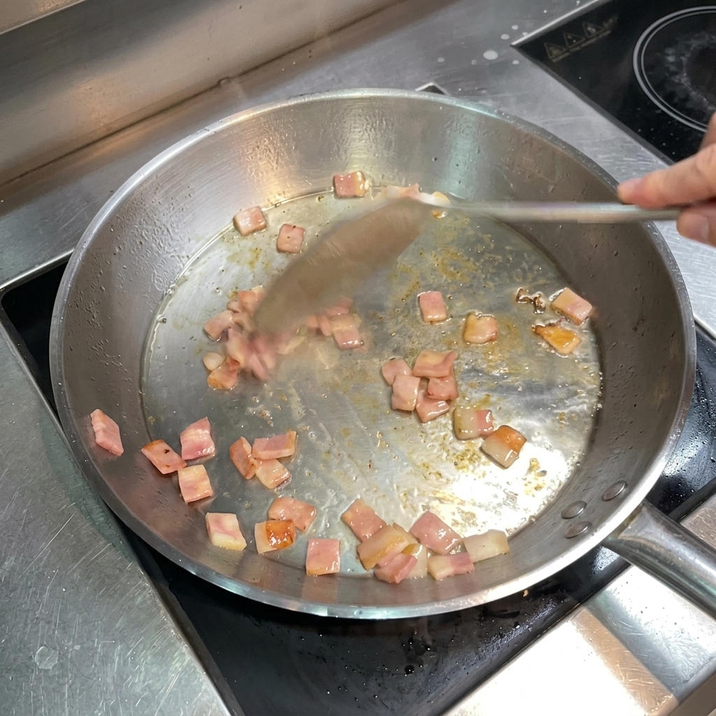 노릇하고 바삭하게 익은 베이컨을 스테인리스 뒤집개로 젓는 모습.