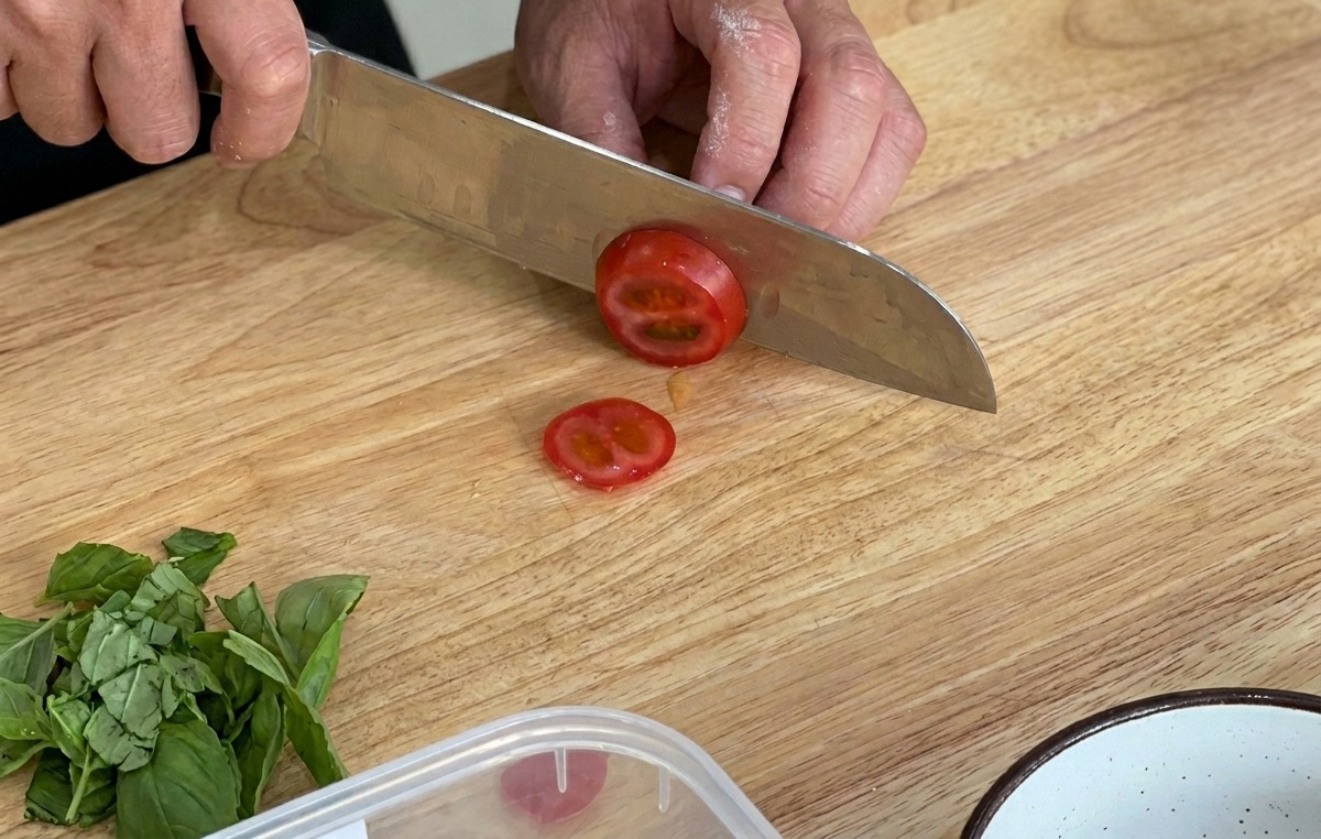 도마 위에서 날카로운 칼로 방울토마토를 얇게 썰고 있는 모습.