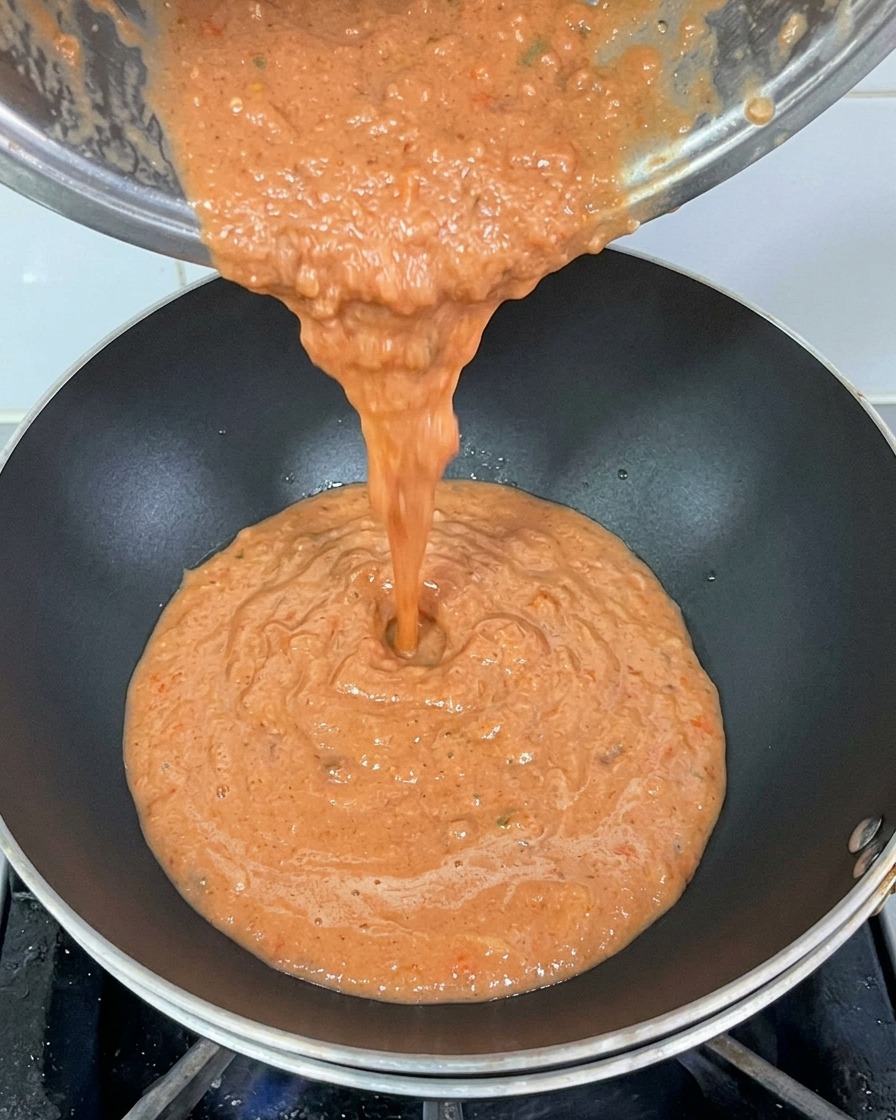 금속 냄비에서 걸쭉하게 갈린 레드 토마토 소스를 달궈진 검은색 웍에 붓는 모습