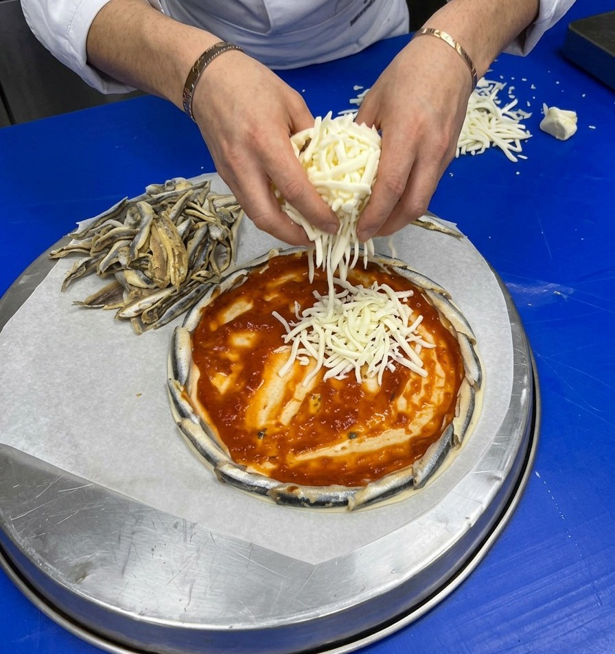 토마토 소스가 발린 피자 도우 위에 갓 갈아낸 화이트 치즈를 듬뿍 뿌리고 있는 손