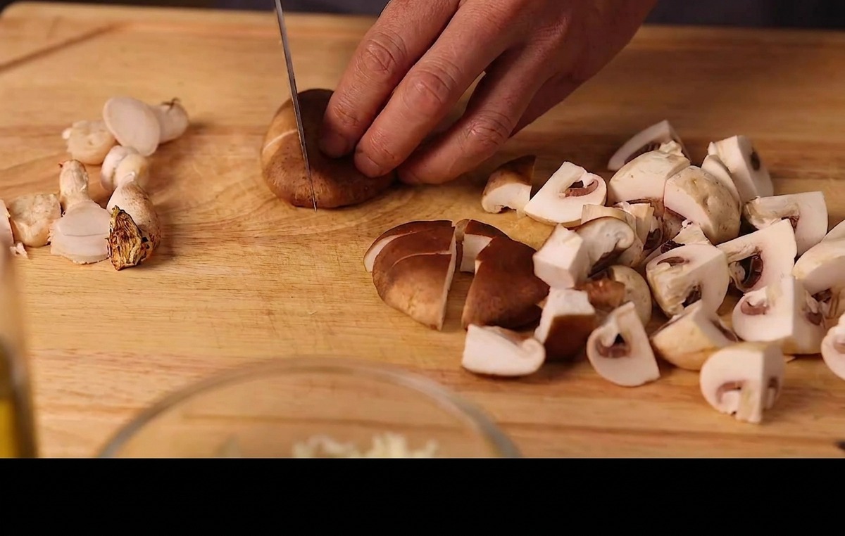 나무 도마 위에서 신선한 표고버섯과 양송이버섯을 적당한 크기로 썰고 있는 모습.