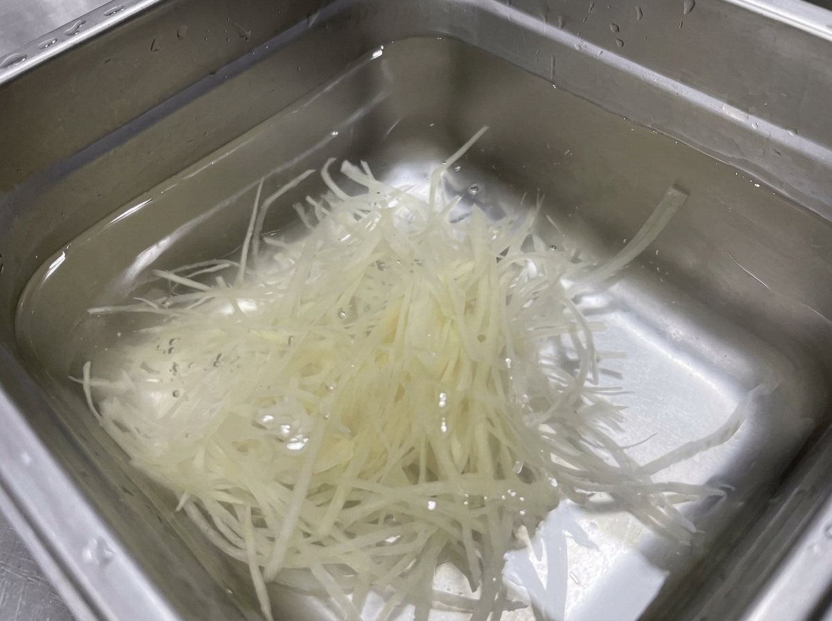 스테인리스 볼에 담긴 깨끗한 물에 잠겨 있는 가느다란 감자채.