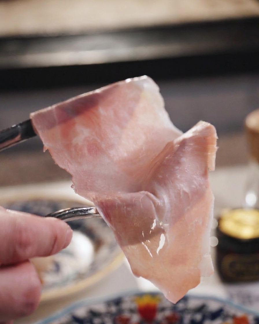 포크로 들어 올린 얇고 반투명한 핑크 햄 조각.