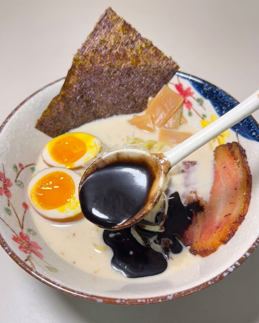 완성된 라멘 위에 진한 검은색 마유를 뿌리는 장면.